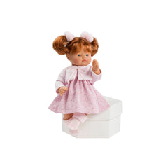 ASI Dolls Guille, 36 cm, with red hair in pigtails, wearing a pink plumeti knitted jacket and socks, seated on a white box.