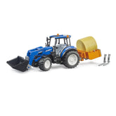 Blue New Holland toy tractor with frontloader, yellow hay bale on trailer, and detached forks, showcasing agricultural play.