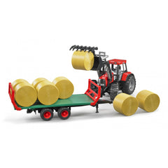 Red toy tractor loading hay bales onto green trailer with red trim, Bruder 1:16 scale play vehicle.