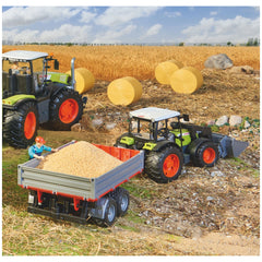 Toy tractor and trailer in a wheat field with hay bales and a worker, showcasing BRUDER's realistic agricultural play set.