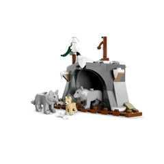 Three toy wolves, two gray and one light brown, are positioned in front of a gray cave structure. A white bone lies on the ground nearby, and a small tree stands atop the cave, completing the Arctic exploration scene.