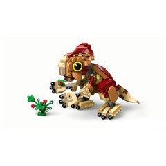 LEGO Baby Dinosaur Dolores, a brick-built Aquilops figure in tan and red colors, sits playfully next to a buildable plant with colorful flowers.