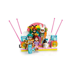 A vibrant LEGO Friends costume party scene featuring four minifigures: Autumn as a bumblebee, Olly as a merman, Leo as a magician, and Paisley in fairy attire, with a DJ booth, colorful backdrop, and playful accessories.