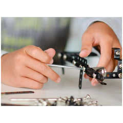 Child assembling a metal construction set with a silver tool, focusing on tiny black perforated pieces.