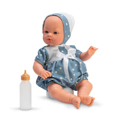 ASI Dolls Koke Ranita, 36 cm, in blue daisy outfit with white bow, sits beside a baby bottle.