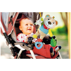 Baby Clementoni soft bear stuffed animal is held by a smiling child in a stroller, surrounded by greenery outdoors.