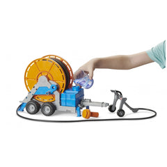 Child's hand pouring water into Bruder irrigation trailer toy with orange hose reel and blue tank.