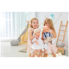 Heless blue sneakers for dolls displayed in a bright room with two girls in pink dresses and a yellow tent in the background.