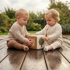 Jollein Activity Cube features two children in knitted clothing engaging with a tree-design cardboard box on a wooden surface