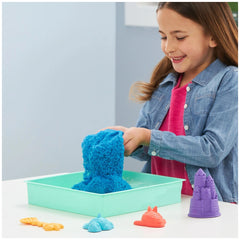Kinetic Sand Sandbox Set features a young girl pouring blue sand into a green tray, surrounded by orange and purple materials