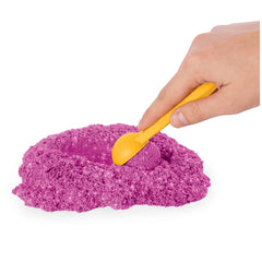 Kinetic Sand Shimmer Sparkle Sandcastle Set features a human hand holding a yellow spoon with purple sand on it.