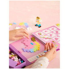 Plus Plus Fairytale Activity Pad held by hands on a pink surface, featuring colorful plastic puzzle pieces and a star-pattern