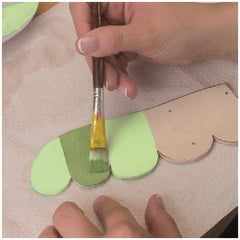 Hand painting a wooden craft piece with green paint using a brush on a paper towel.