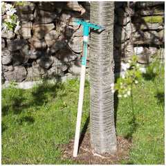 Theo Klein Bosch garden rake positioned in a lifestyle scene with green grass, a brown wooden fence, and a gray tree trunk.
