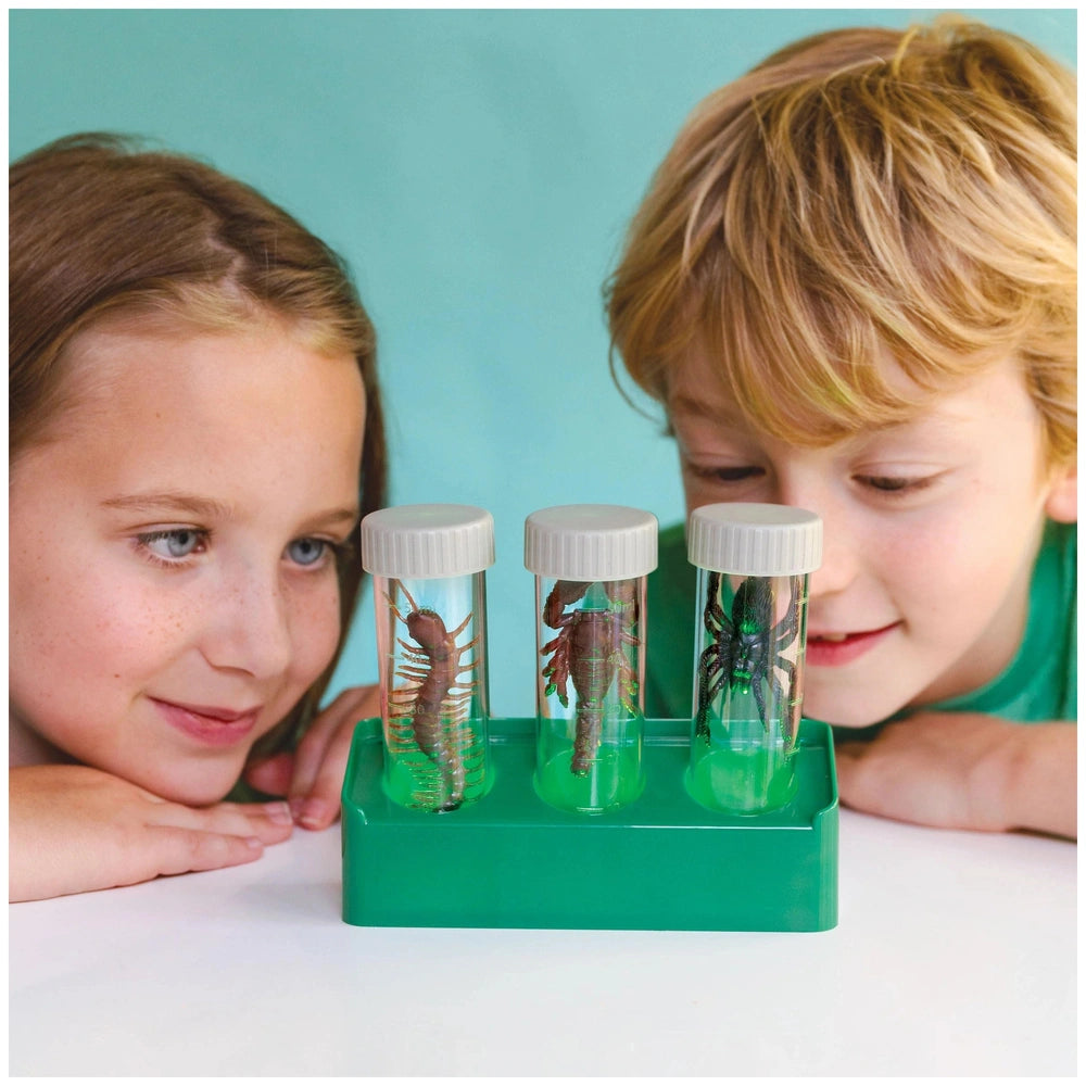 KidzLabs Glow Critter Lab toy playset displayed on a white table with two children wearing green shirts in a light blue backg
