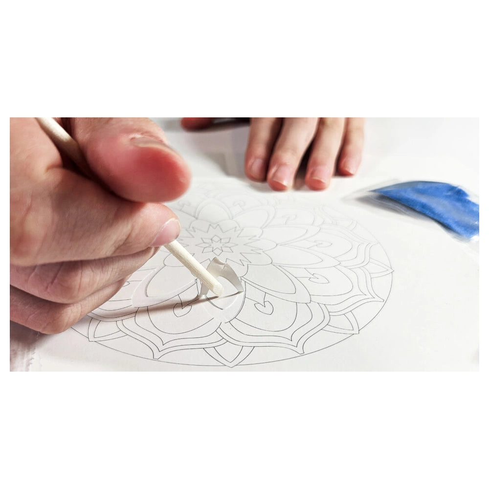 Sand Art Mandala kit with a person's hands drawing on patterned paper using a pencil and a blue paintbrush.