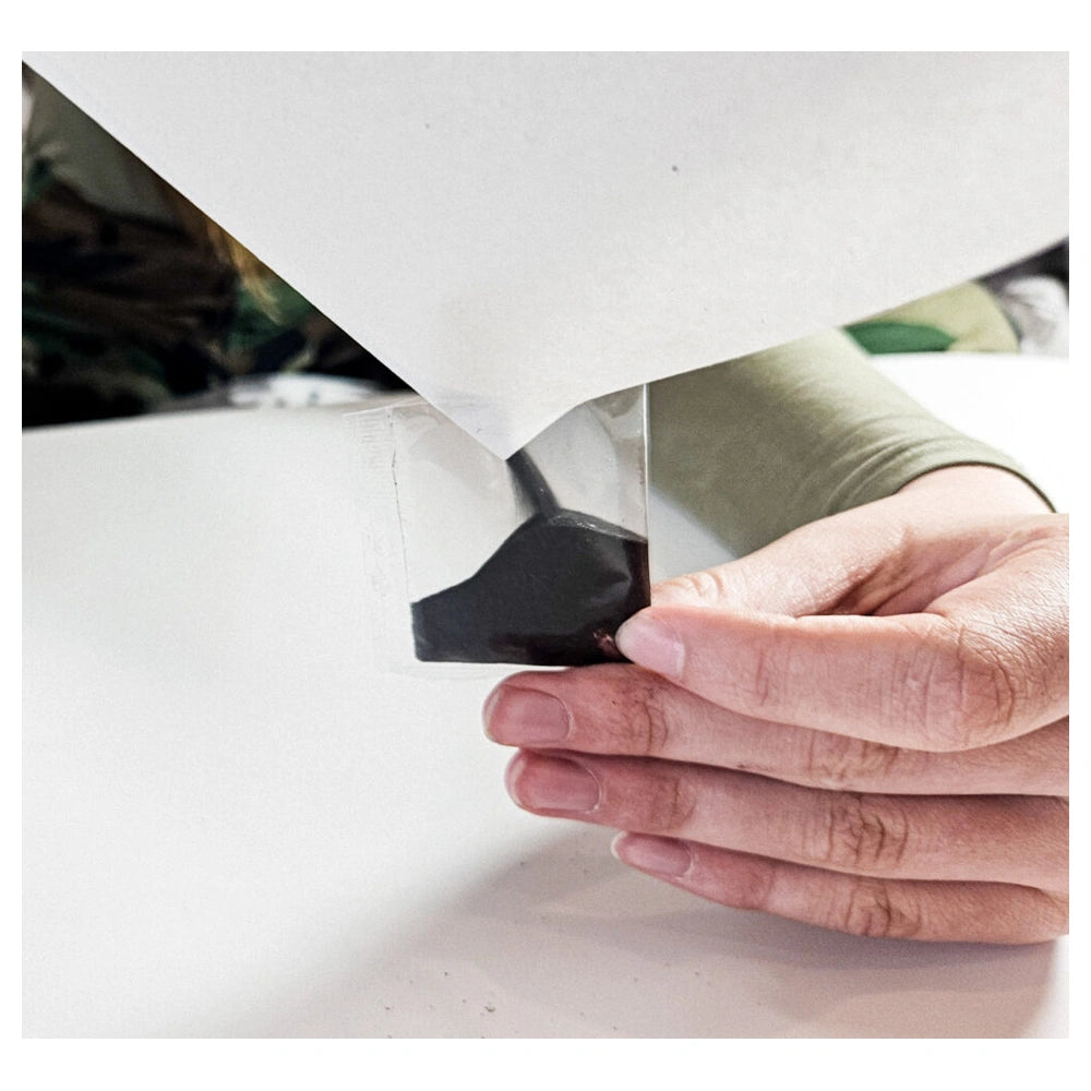 A hand holds a small dark object against a smooth white surface in a blurred indoor setting.