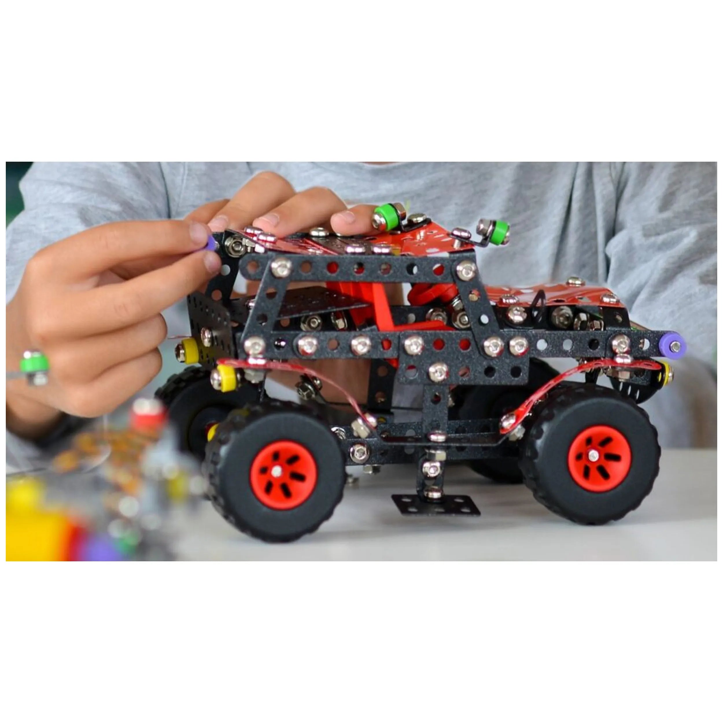 Child assembling Alexander Constructor Black Spider off-road toy with metal and red plastic pieces on table.