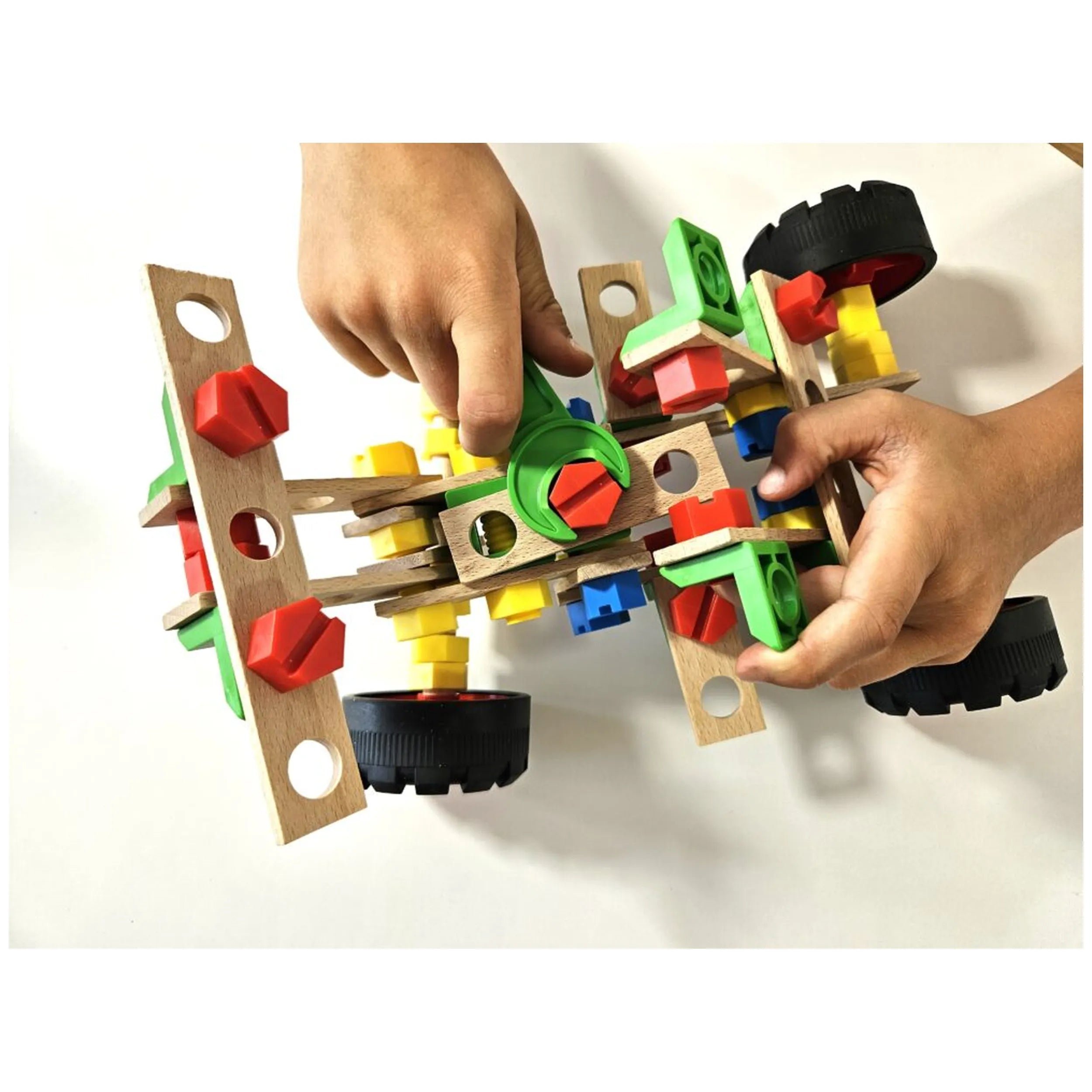 Child assembling colorful wooden buggy with large wheels, using red, green, and yellow pieces in the Maly Constructor set.