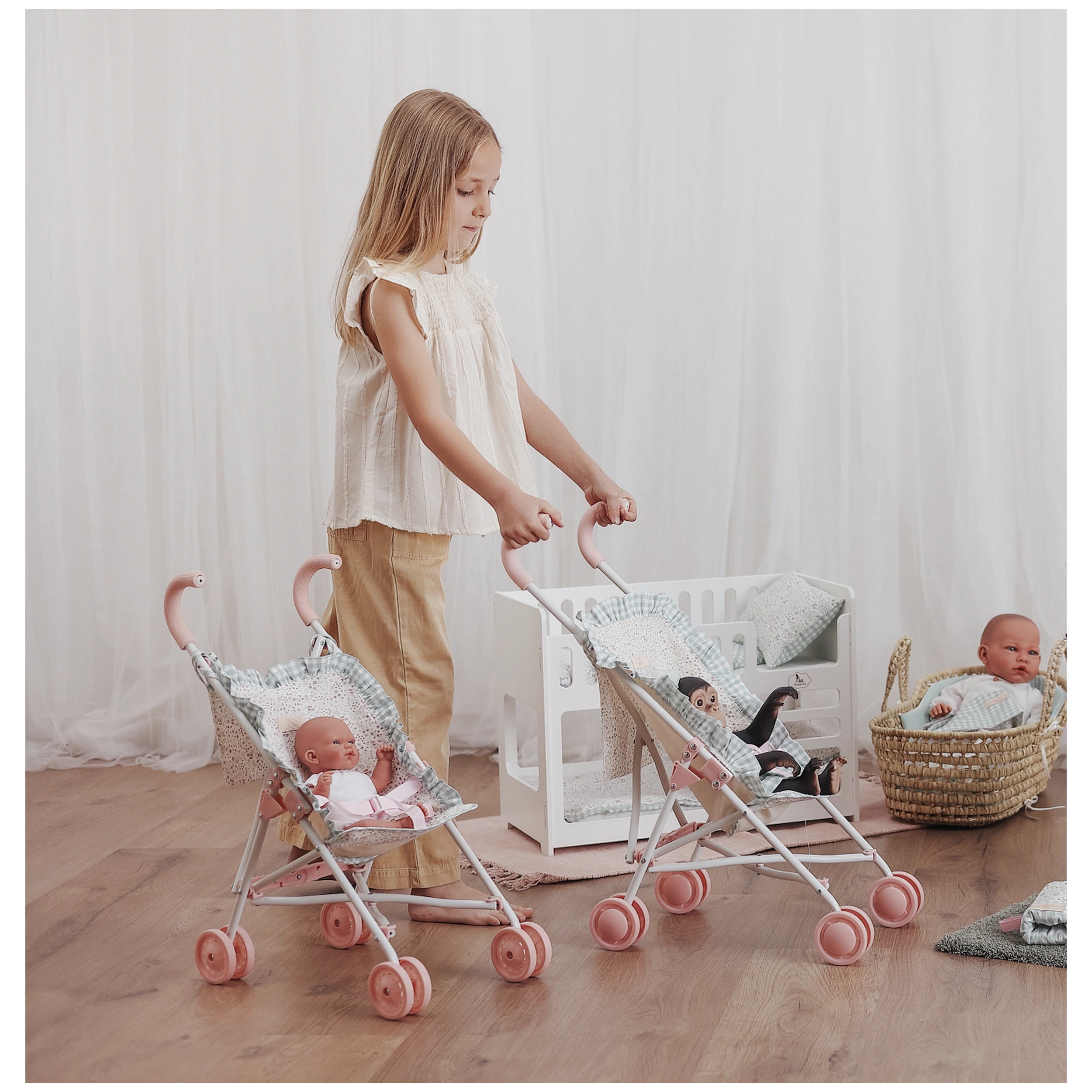 Child playing with pink-handled strollers from ASI Dolls Cloe Collection, each holding a doll, in a softly lit, cozy room.