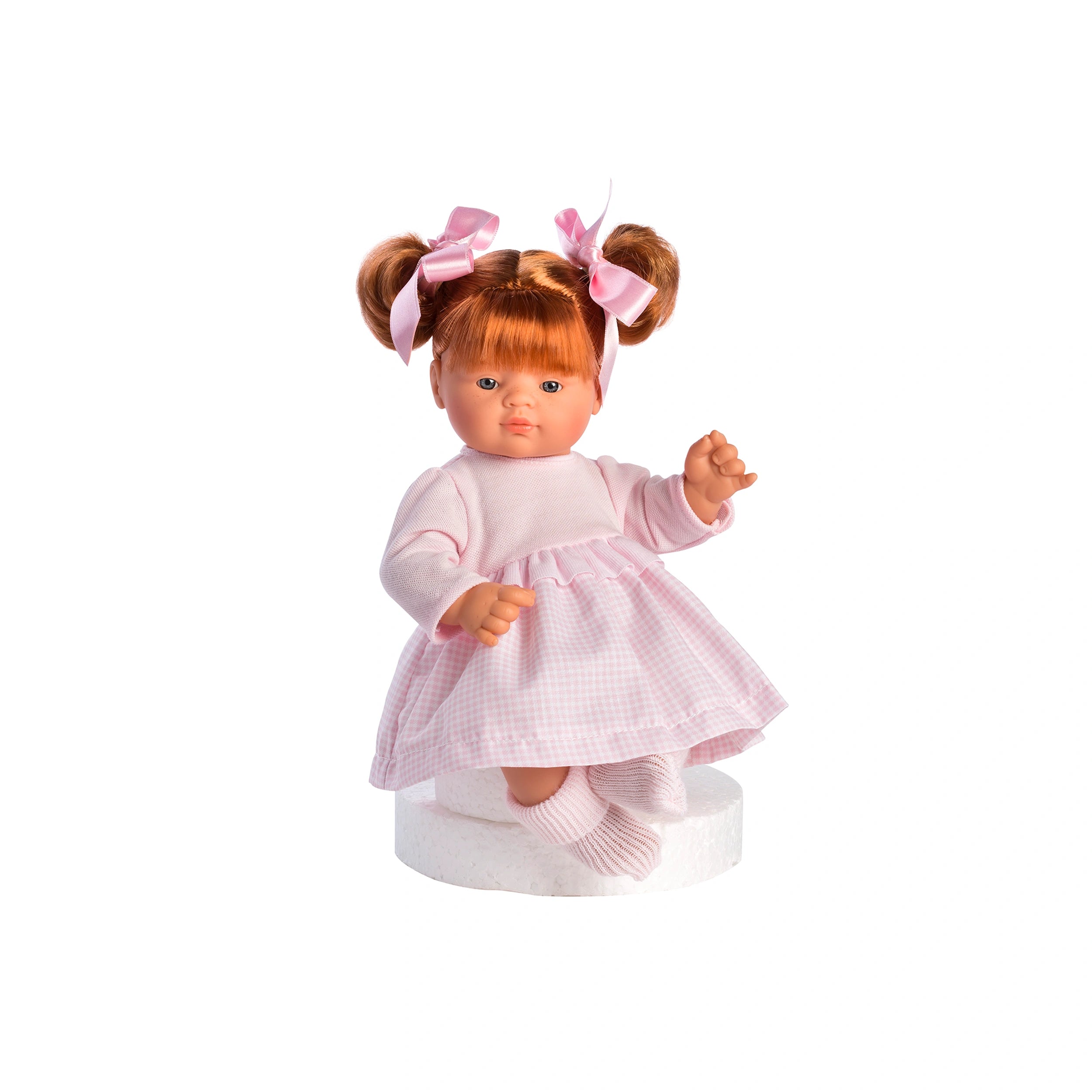 Guille doll with red hair pigtails, pink vichy dress, soft body, and expressive eyes, sitting on a white stand.