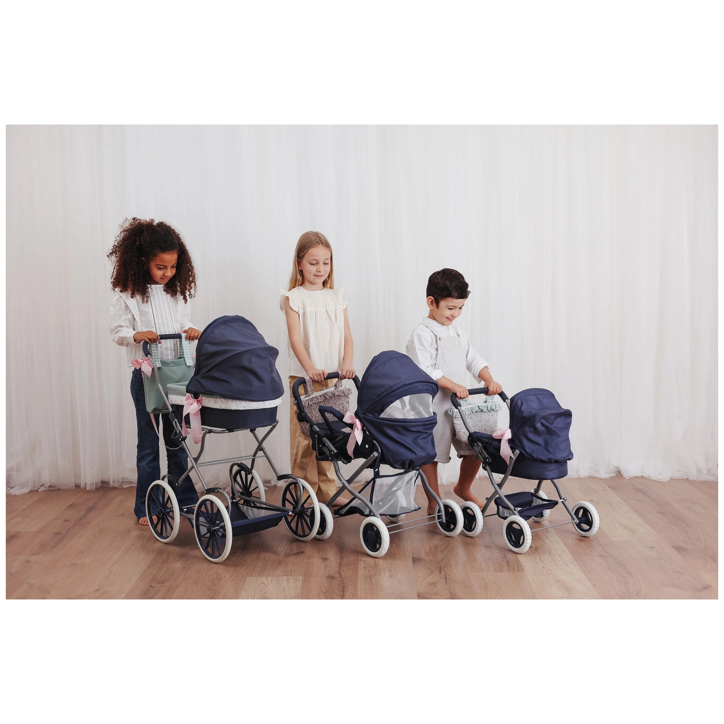 Children engaged in play with navy blue strollers, featuring dolls and accessories, on a wooden floor.