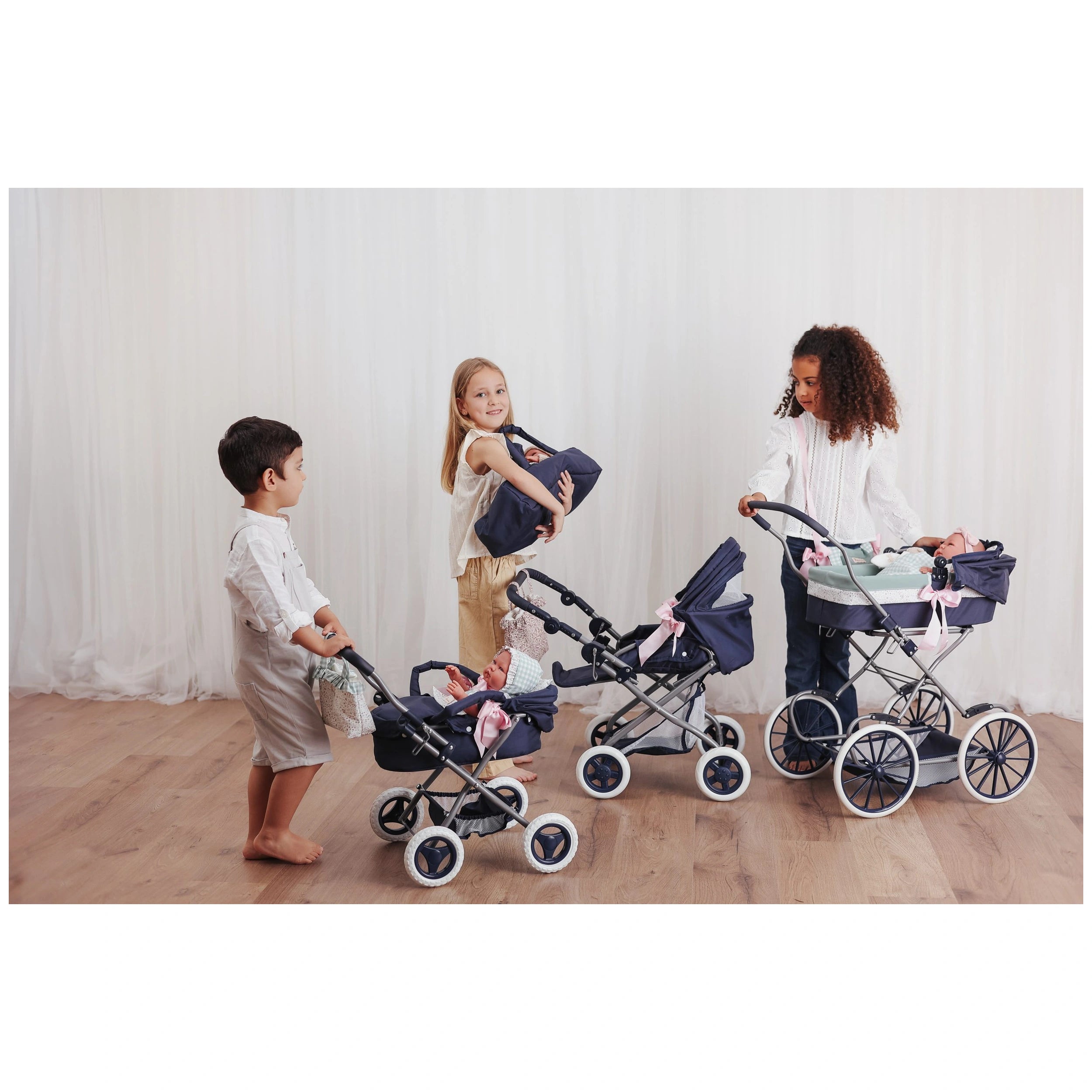 Children play with ASI Dolls Martina Swing strollers in a room, each with a doll and a navy blue diaper bag.