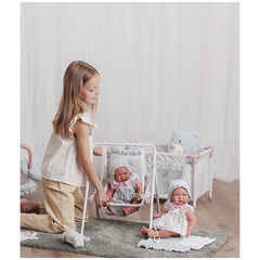 Young girl playing with Asi Dolls Pablo in a swing and on a rug, in a cozy room with a teddy bear in the background.