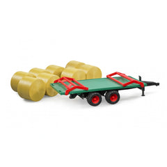 Green and red Bruder bale transport trailer with eight yellow round bales on white background.