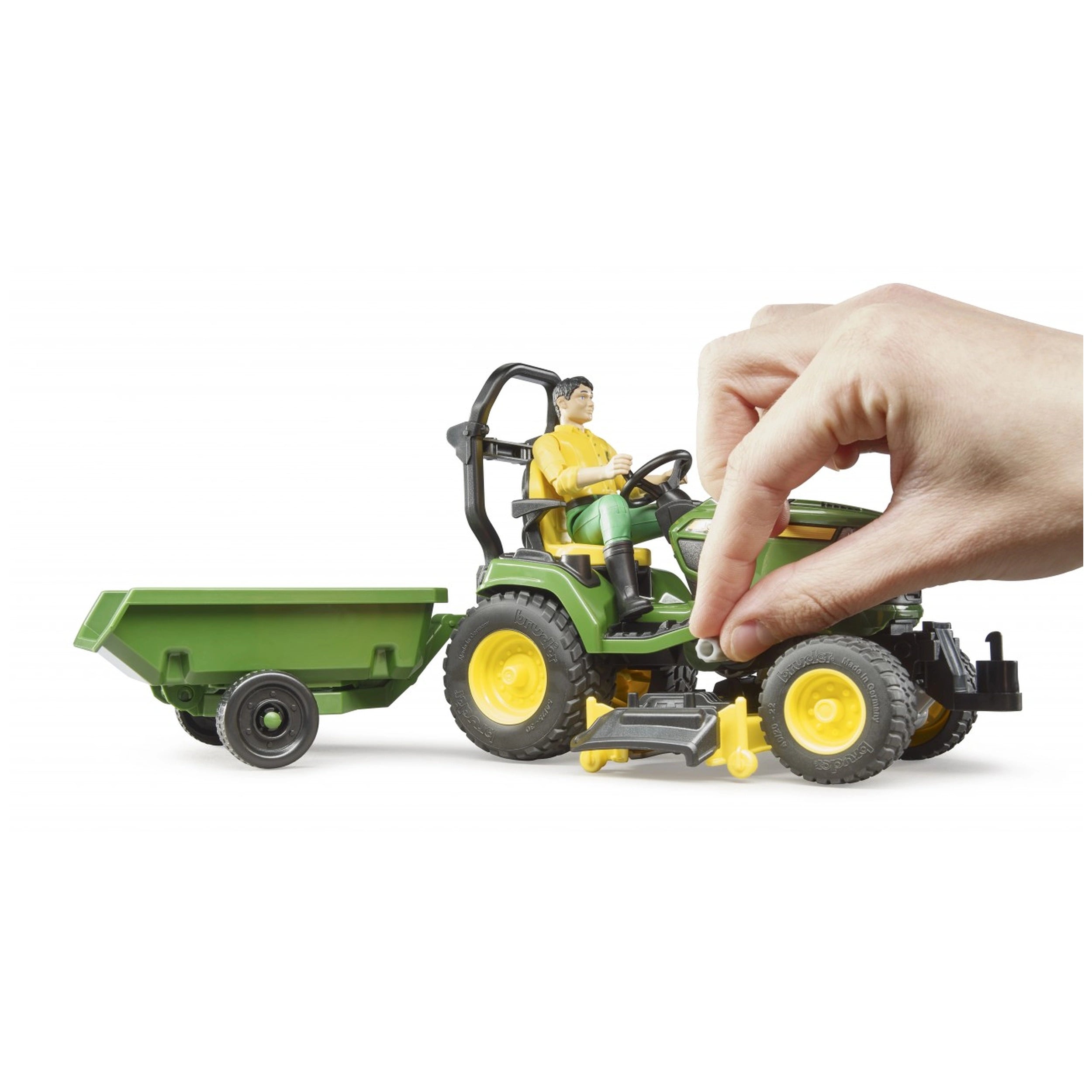 Hand adjusting John Deere lawn tractor toy with trailer and figure, featuring vibrant green and yellow details.