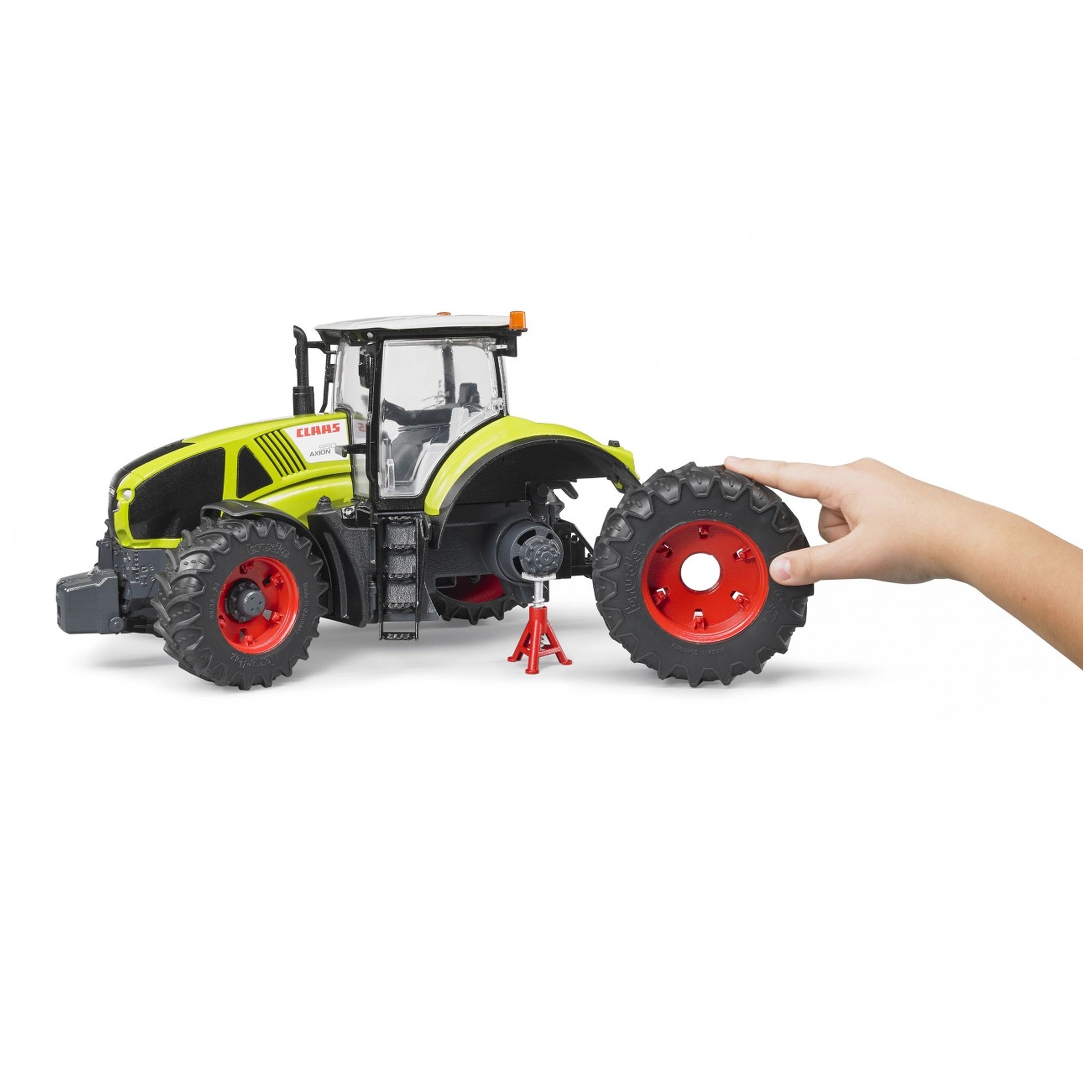 Hand placing a large wheel on a realistic green and black Claas Axion 950 toy tractor with red accents.