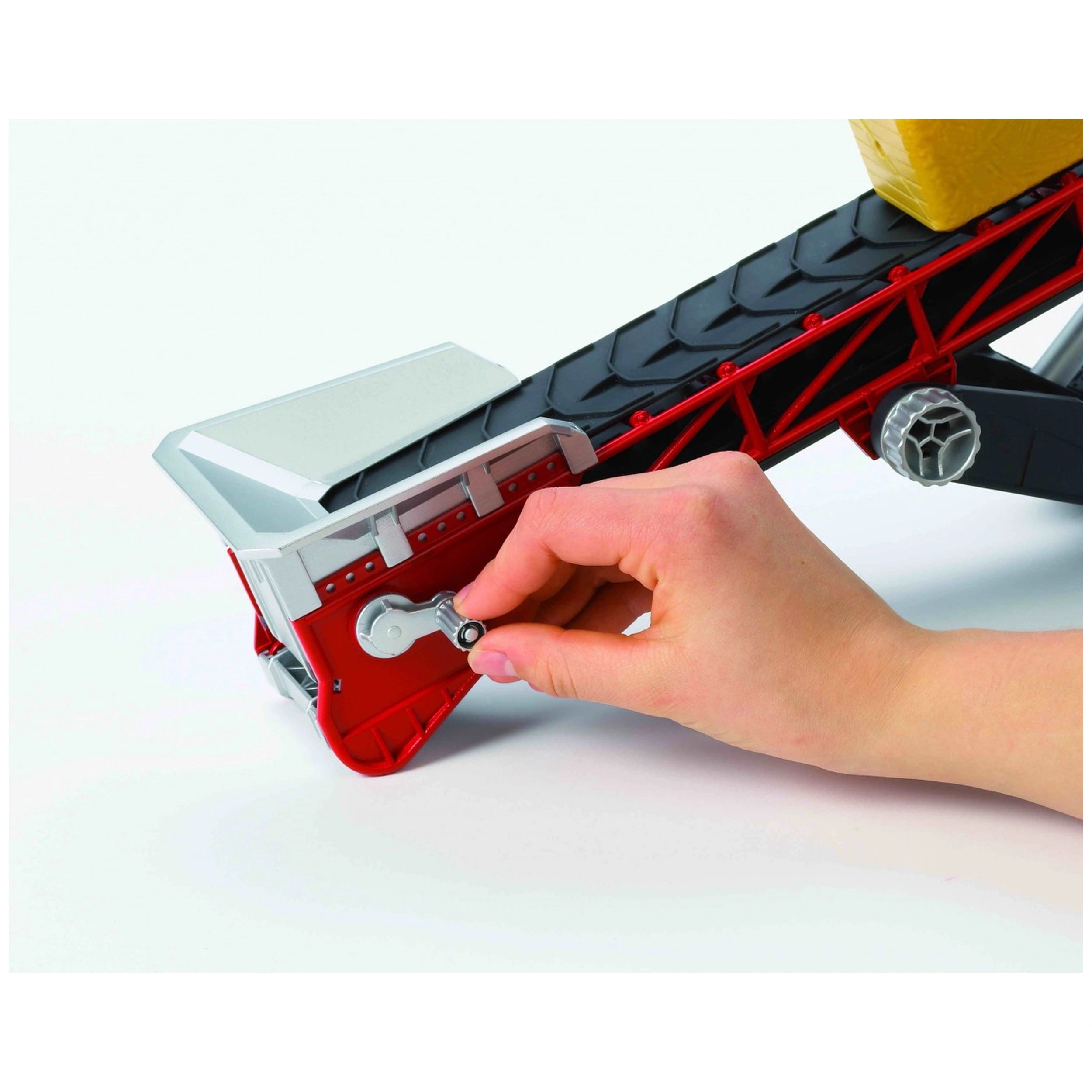 Hand turning crank on red and black Bruder Conveyor Belt toy with hay bale.
