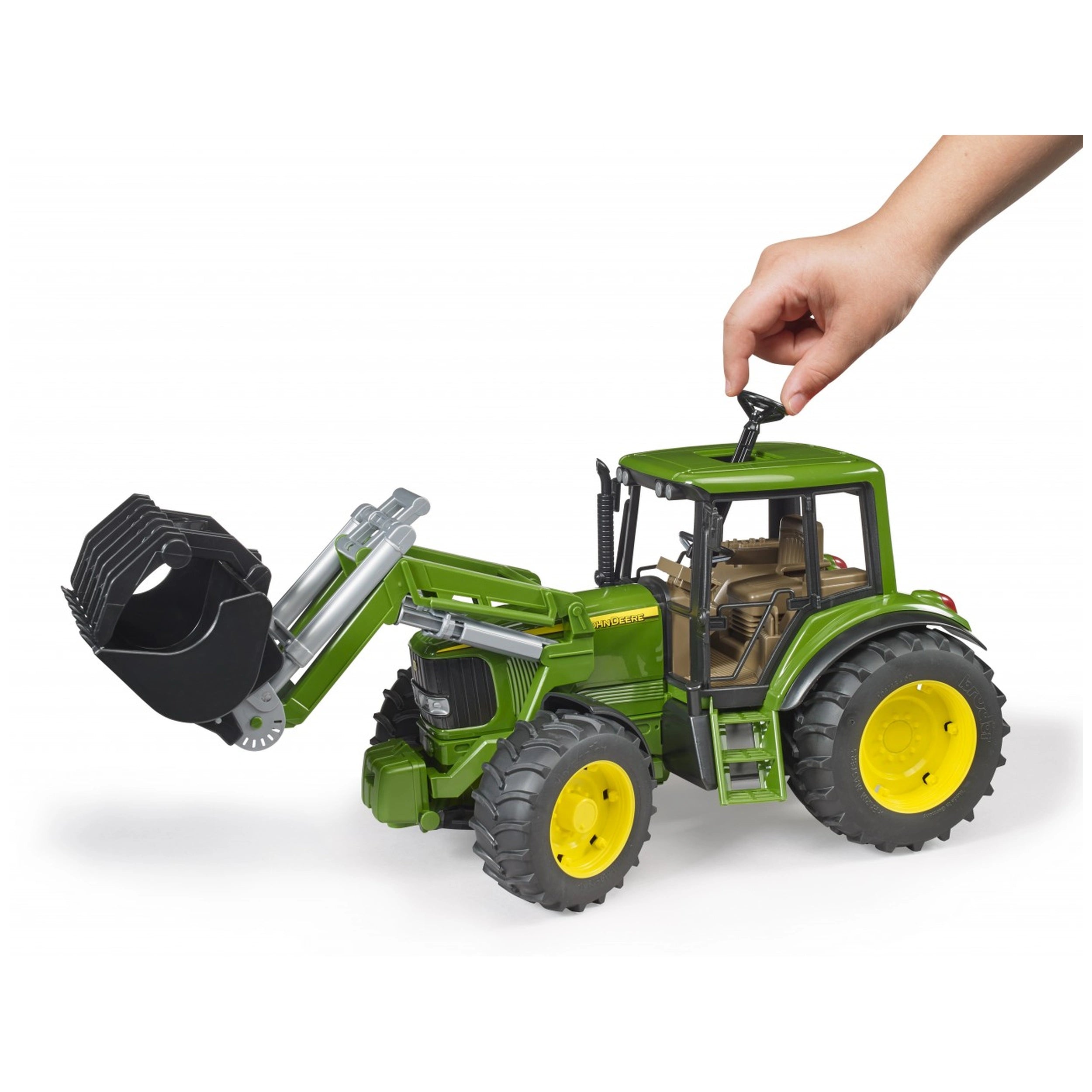 Hand operating the steering of a green Bruder John Deere 6920 toy tractor with a frontloader.