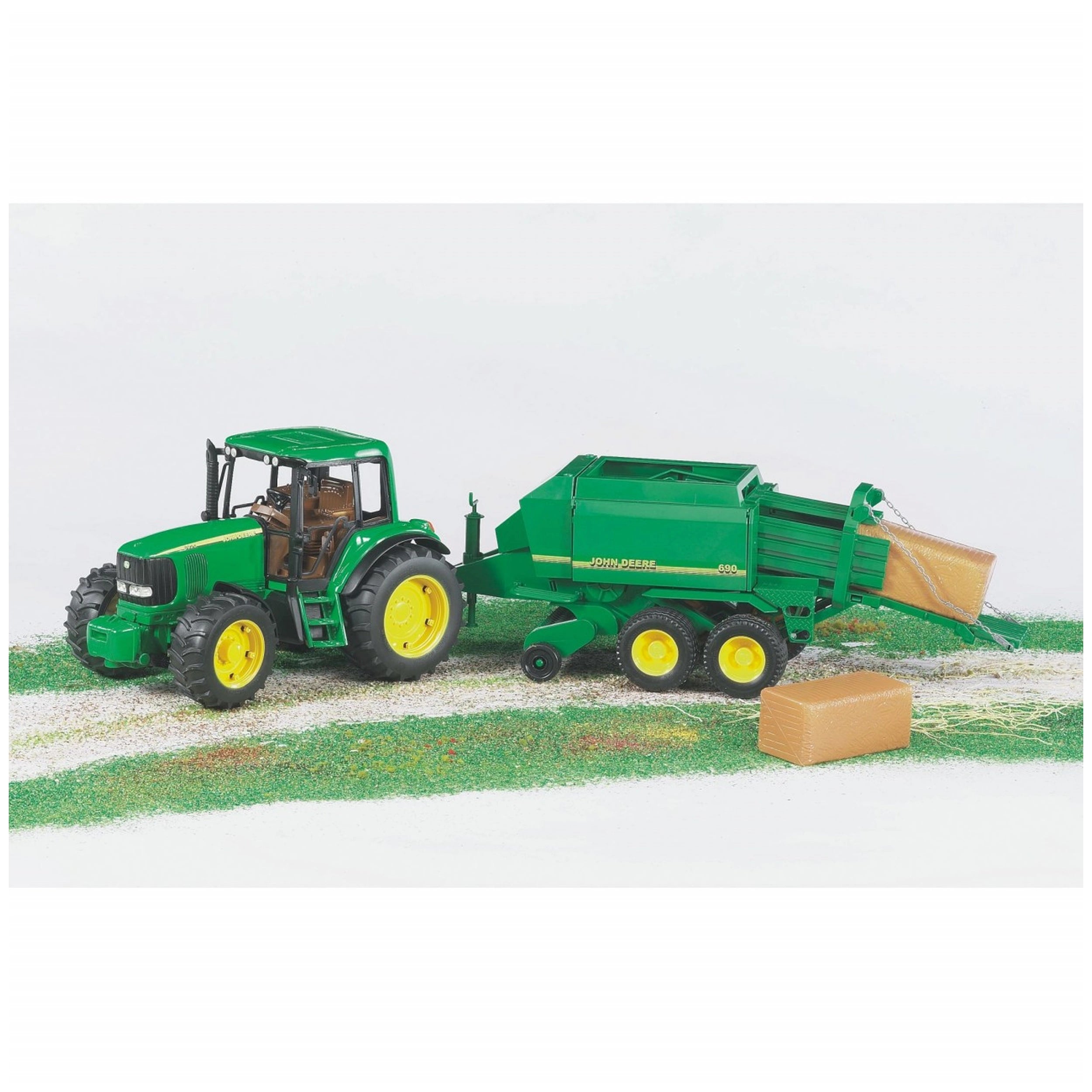 John Deere green toy tractor with yellow wheels and balepress on a field, producing a hay bale.
