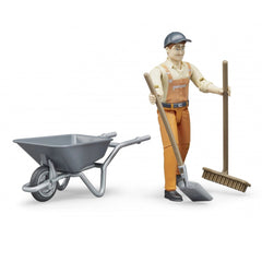 Toy municipal worker figure in orange overalls with gray cap, holding a broom and shovel beside a gray wheelbarrow.