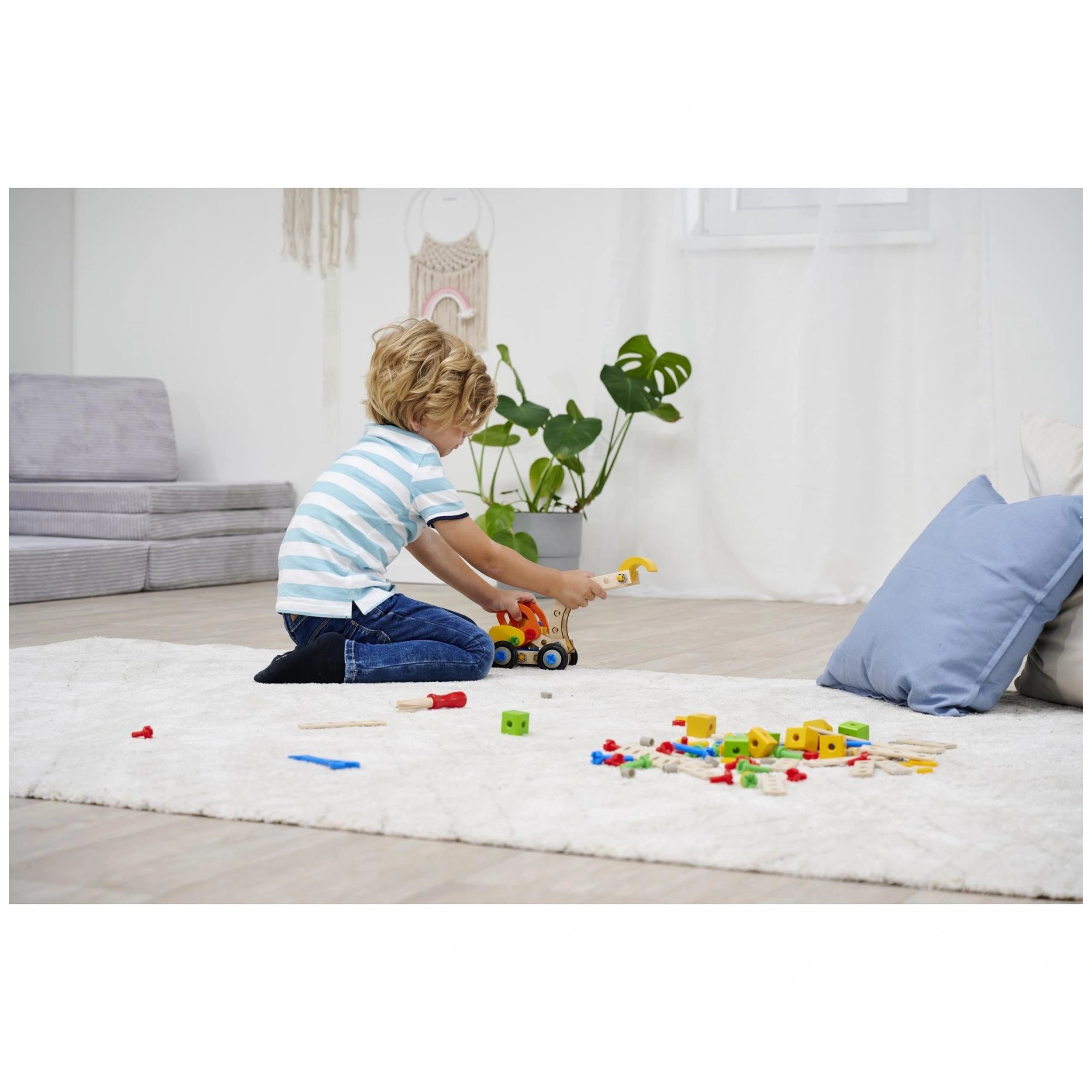 Eichhorn Constructor 3in1 set with a child playing on a soft white surface, holding a yellow toy car beside a blue pillow.