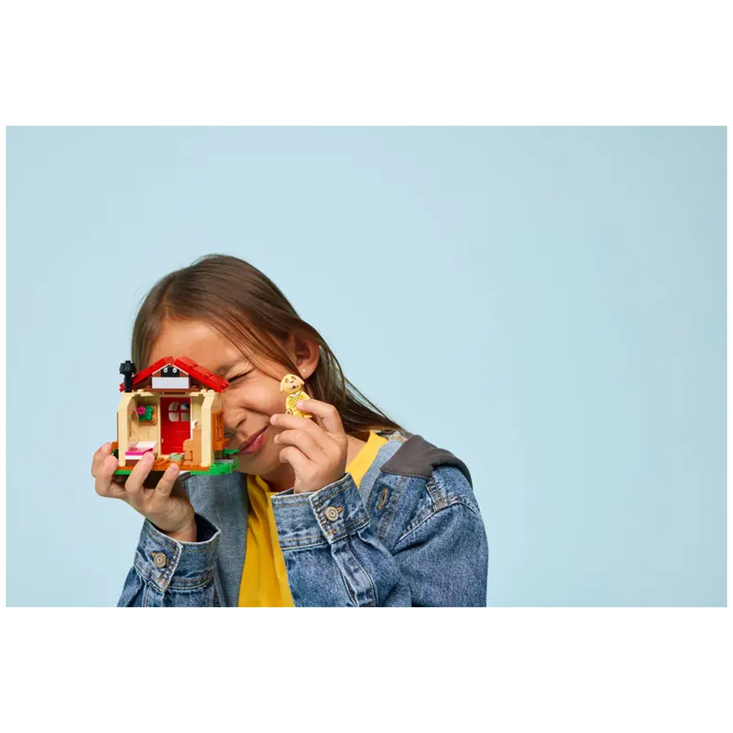 A child smiles while holding the LEGO Animal Crossing Goldie's Cozy House construction set, showcasing the vibrant house and a minifigure.