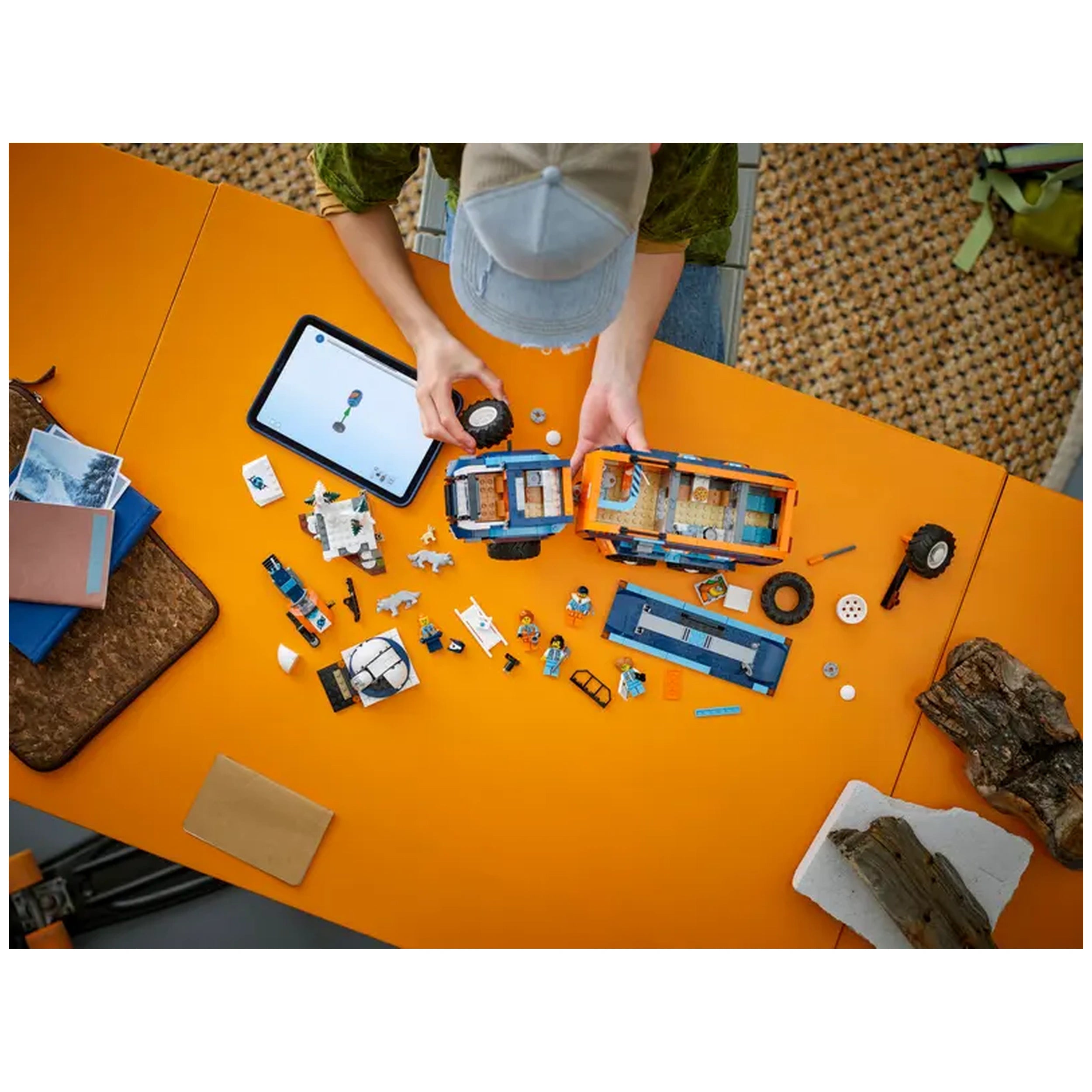 A person assembling the LEGO Arctic Explorer Science Lab Truck on an orange table, surrounded by various LEGO pieces, tools, and an instruction tablet.