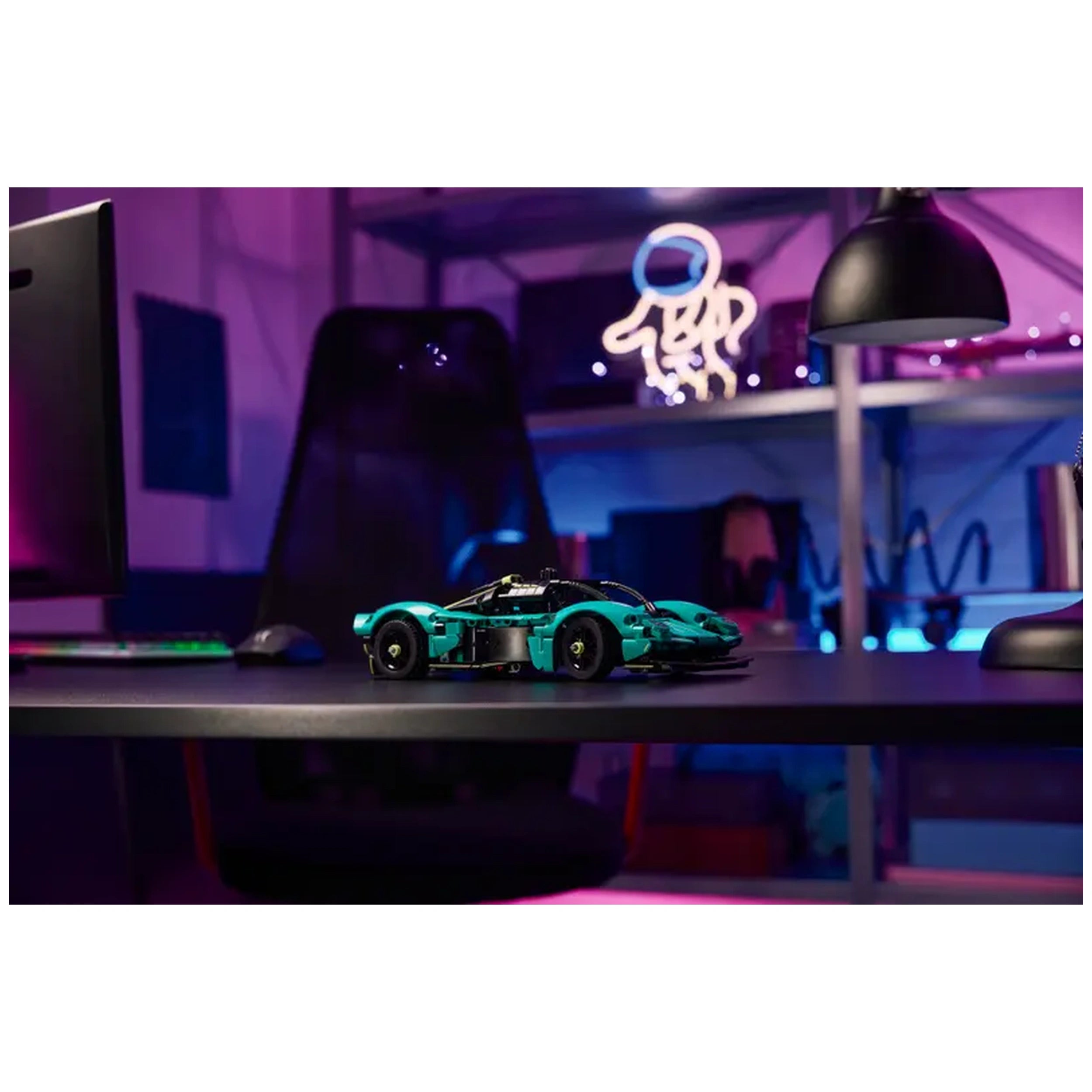 A turquoise LEGO Aston Martin Valkyrie model on a sleek desk, with a computer monitor and stylish lamp in a colorful, modern workspace.