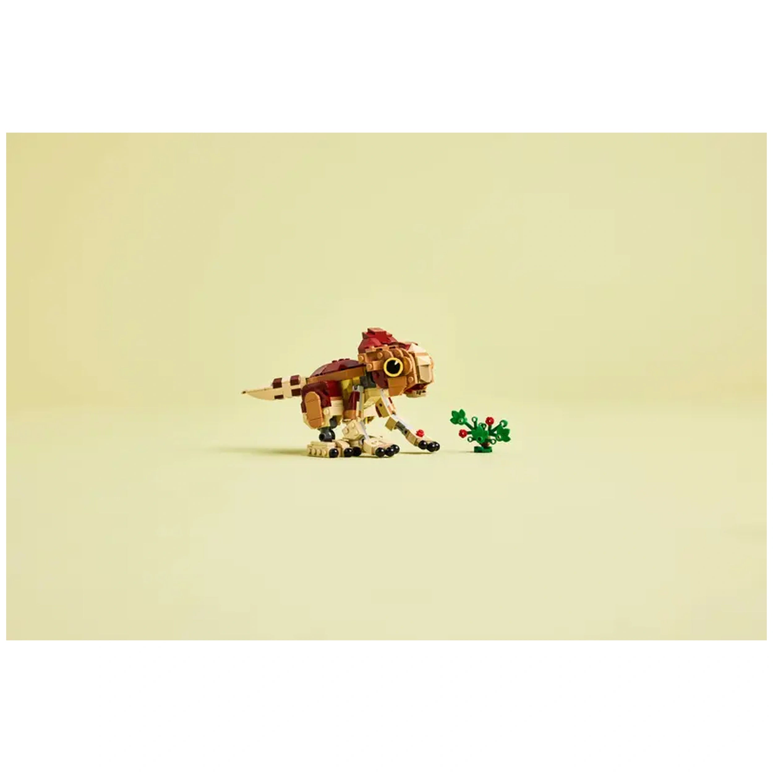 A colorful LEGO Baby Dinosaur Dolores figurine sits on a light background, playfully posed beside a small buildable plant with vibrant flowers. The dinosaur features movable parts, including arms, legs, and a tail, showcasing its intricate design.