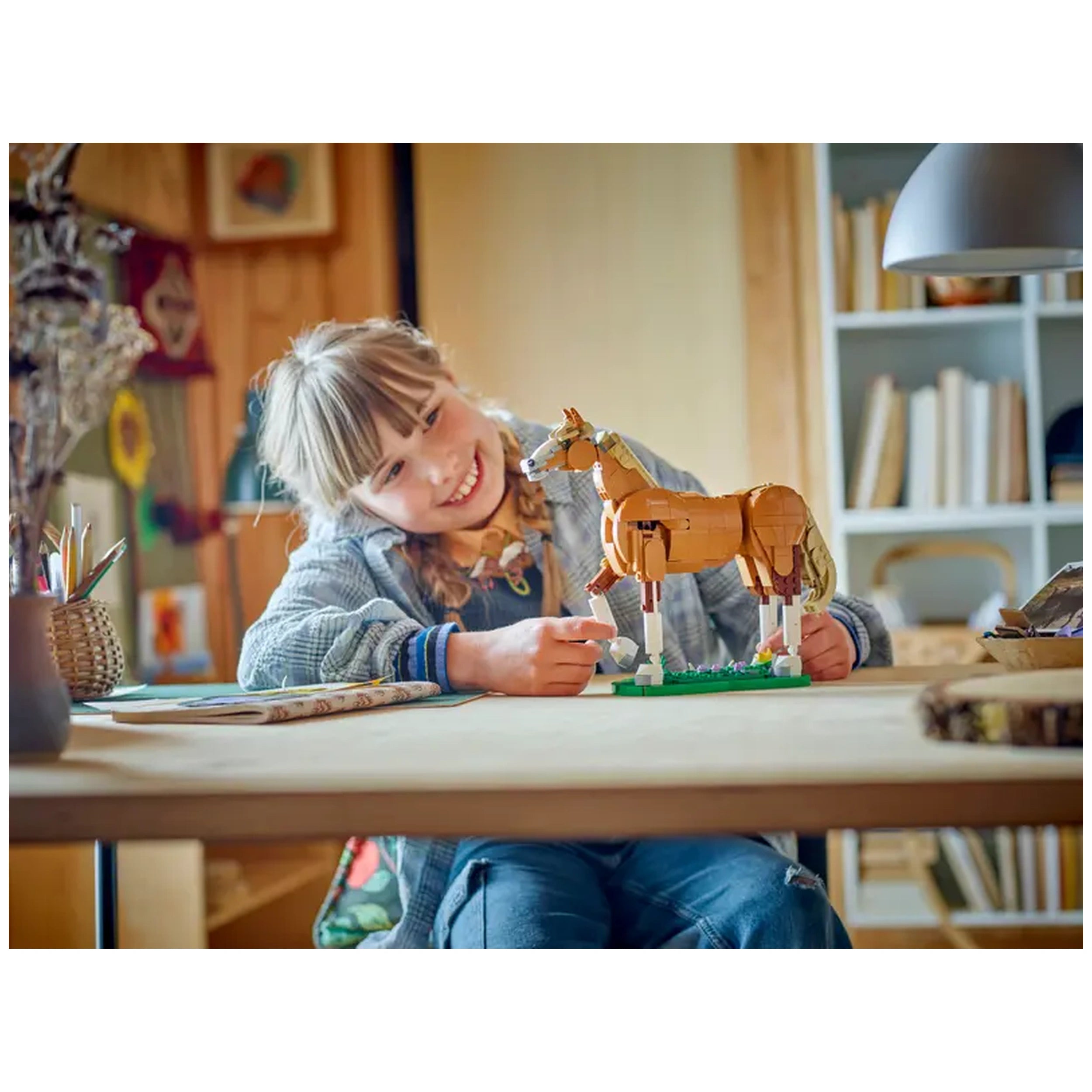 A child smiles while interacting with a LEGO Creator Beautiful Horse set on a wooden table, showcasing the posable horse figure.