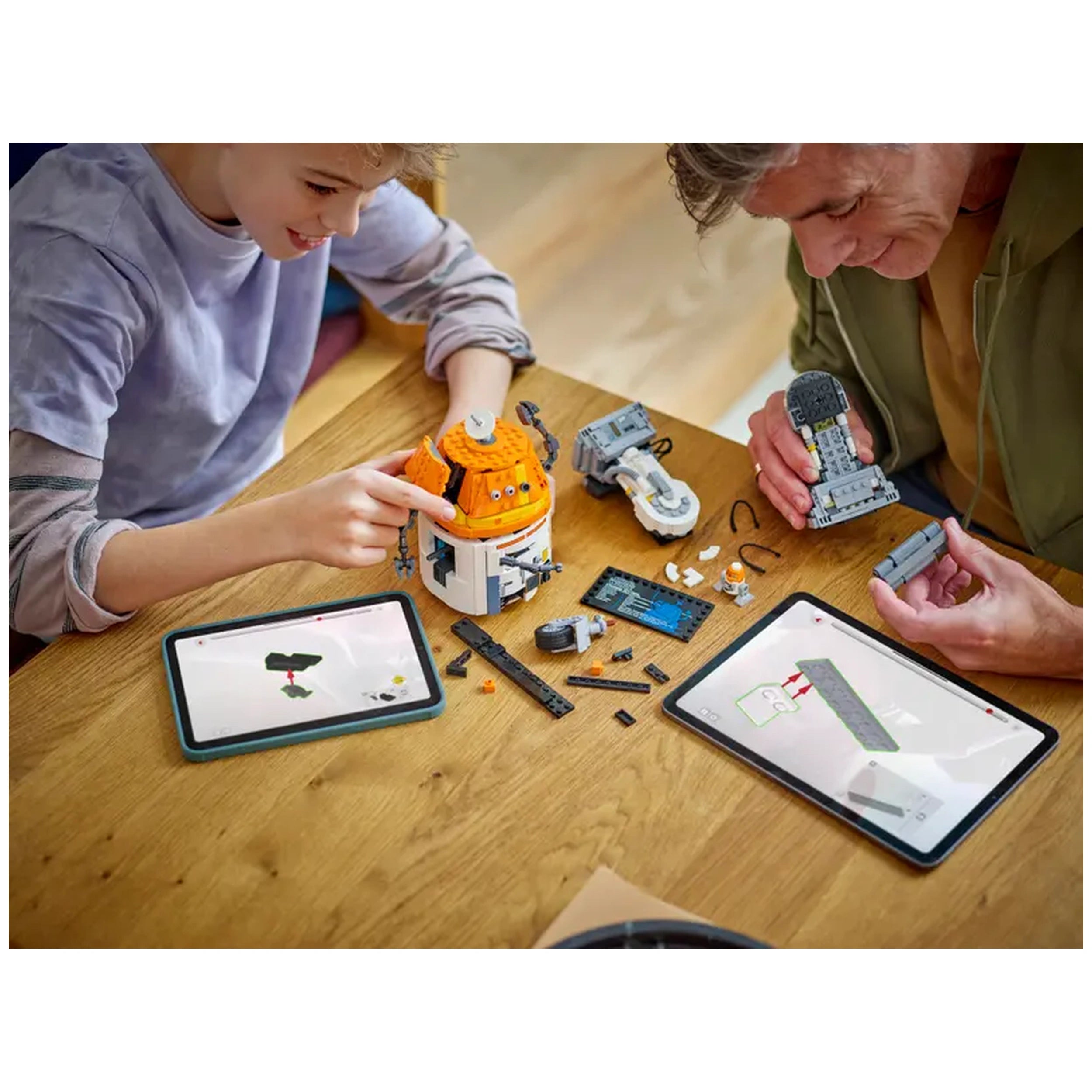 A child and an adult happily building the LEGO Chopper construction set on a wooden table, surrounded by various LEGO pieces and tablets displaying building instructions.