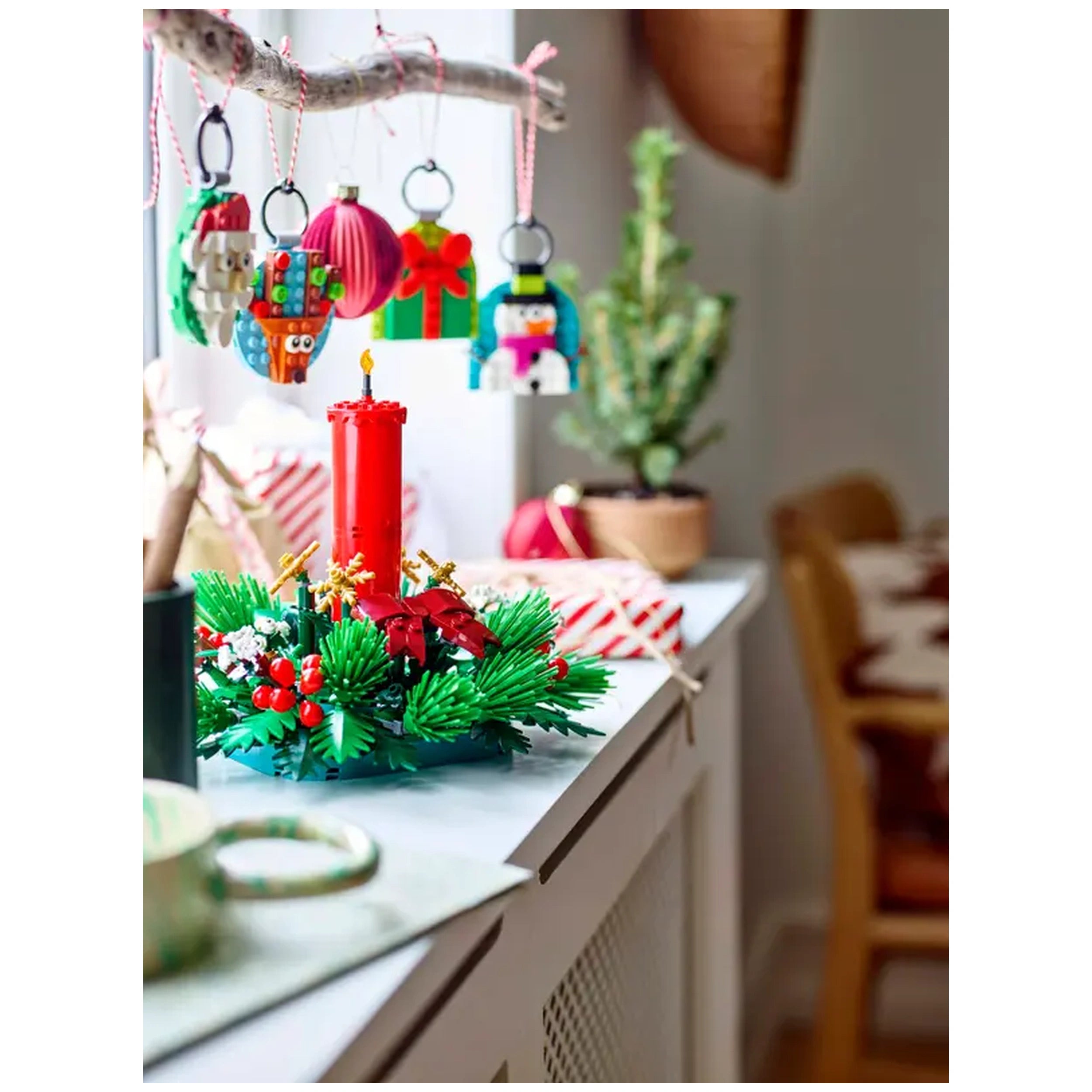 LEGO Christmas Table Decoration featuring a vibrant red candle surrounded by green foliage, red berries, and cheerful ornaments hanging above.