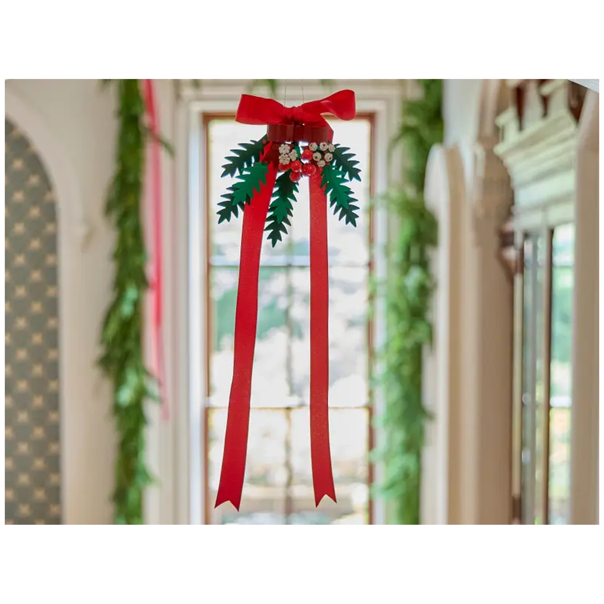 A vibrant holiday decoration featuring a red bow atop green foliage and white berries, hanging centrally in a festive room.
