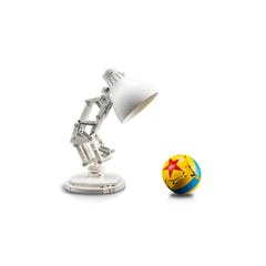 A white articulated lamp with a rounded shade stands beside a colorful, spherical toy ball featuring a yellow base, blue stripes, and a red star. The background is plain white, emphasizing the playful design of both objects.