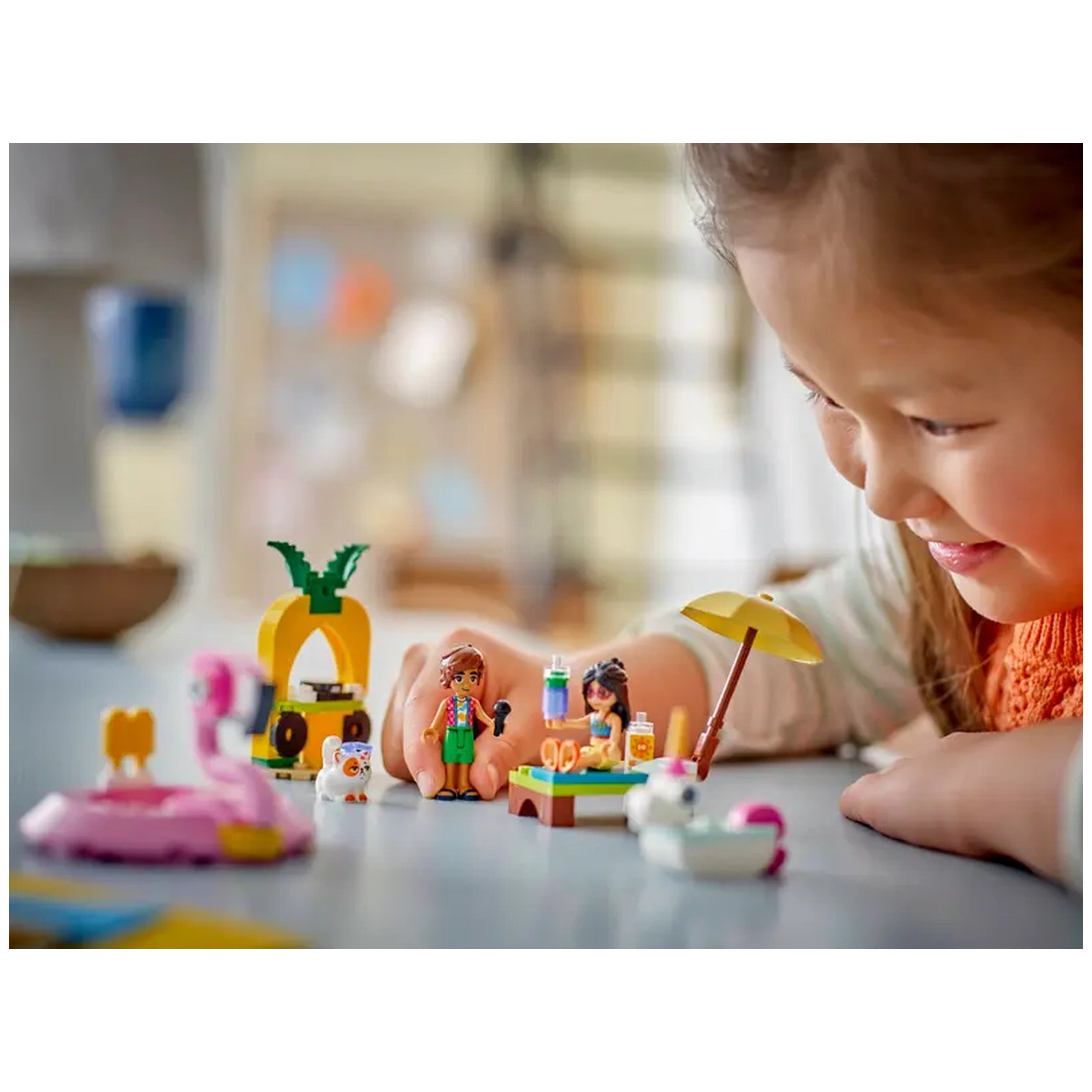 Two LEGO Friends minidolls, Leo and Liann, play at a colorful pool party setup with drinks and floaties while a child smiles nearby.