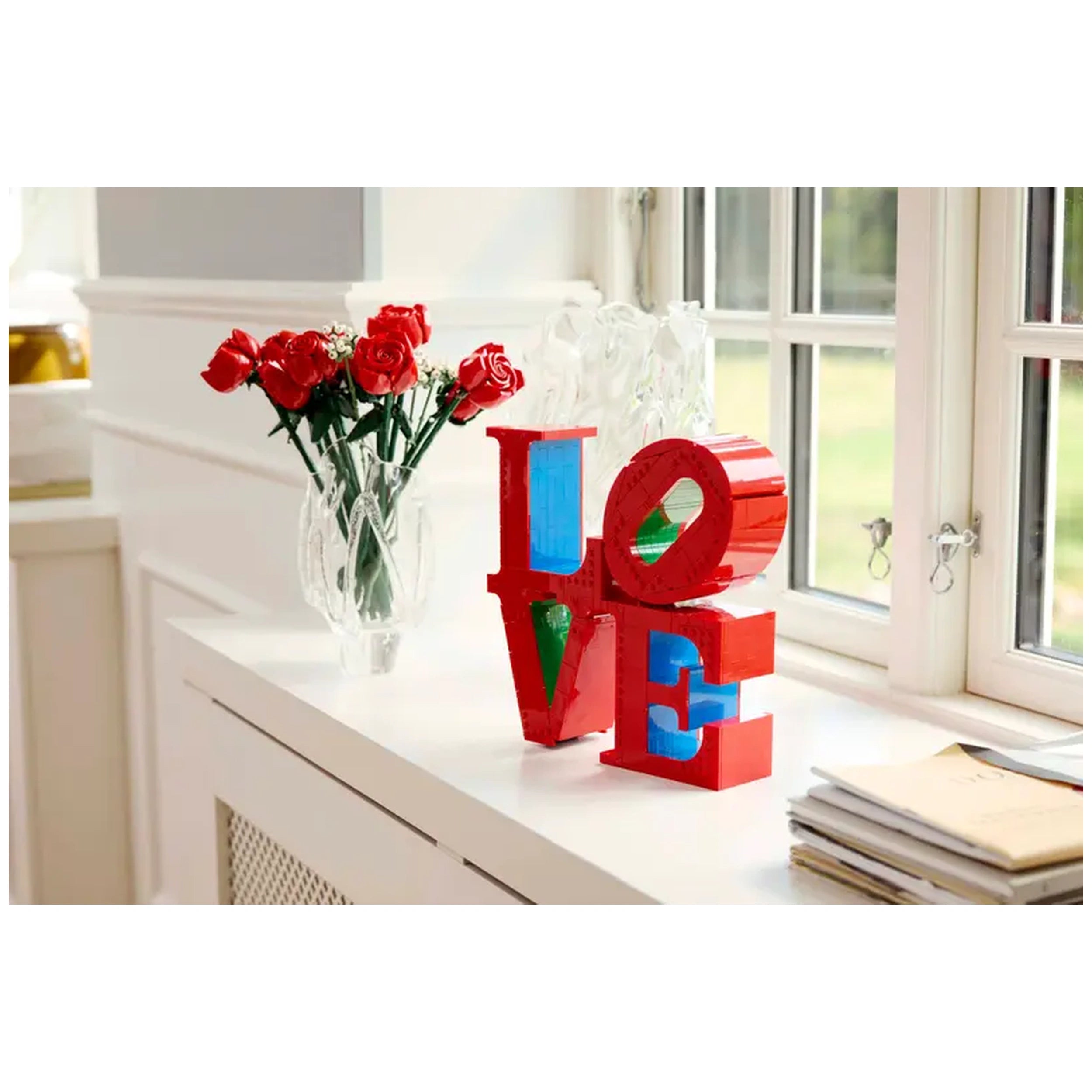 Colorful LEGO® Art LOVE set stands on a white surface, with red roses in a clear vase nearby and sunlight streaming through the windows.