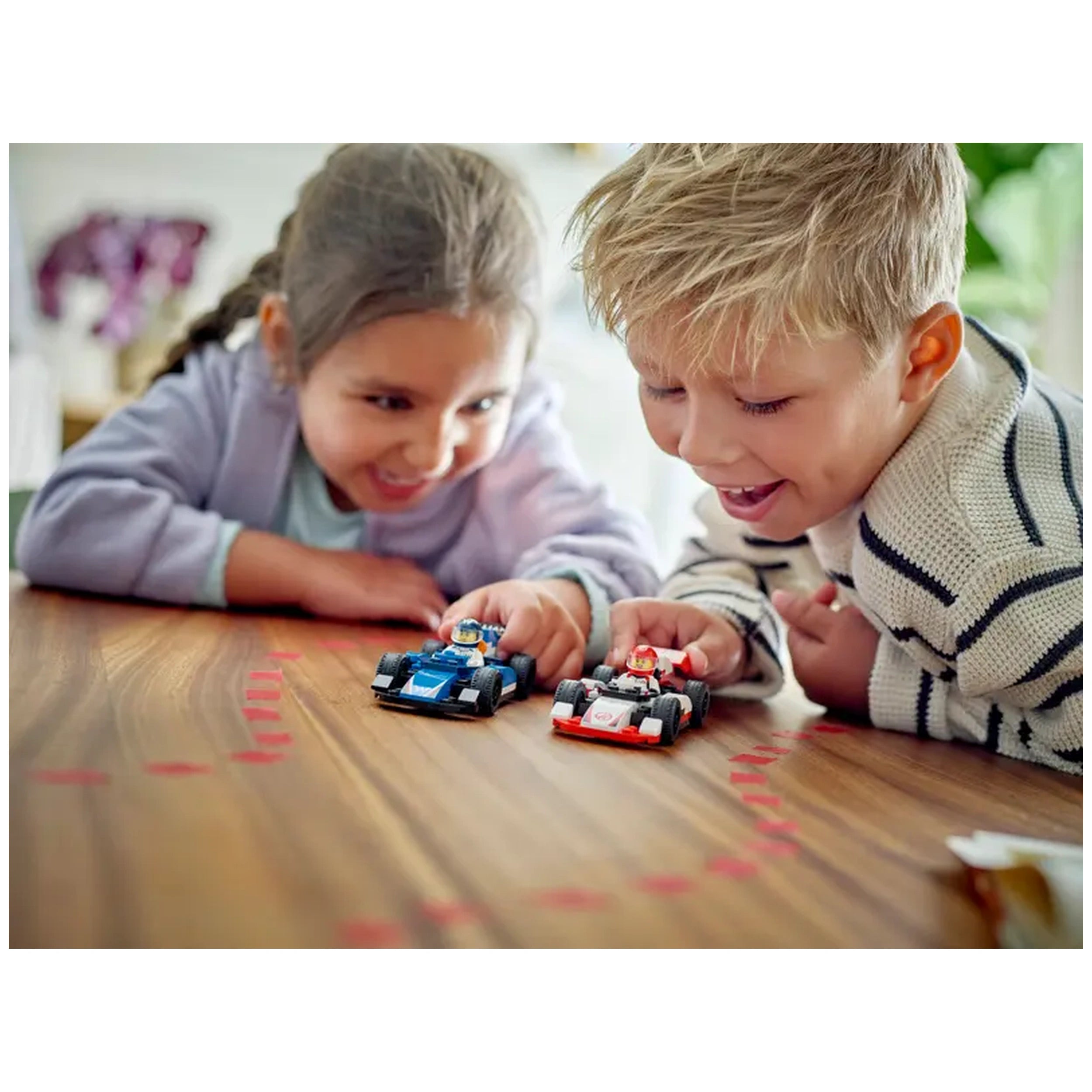Two children excitedly play with LEGO® F1® race cars on a wooden table, focusing on the blue and red cars with driver minifigures.