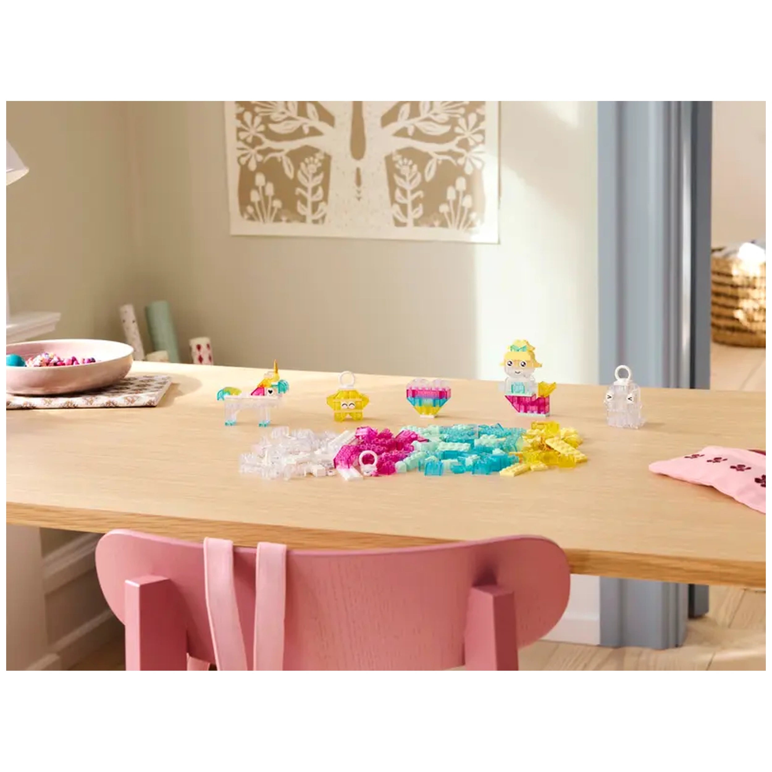 Colorful LEGO® pieces arranged on a wooden table, including transparent stars, a unicorn, and various whimsical creations, with a pink chair in view.