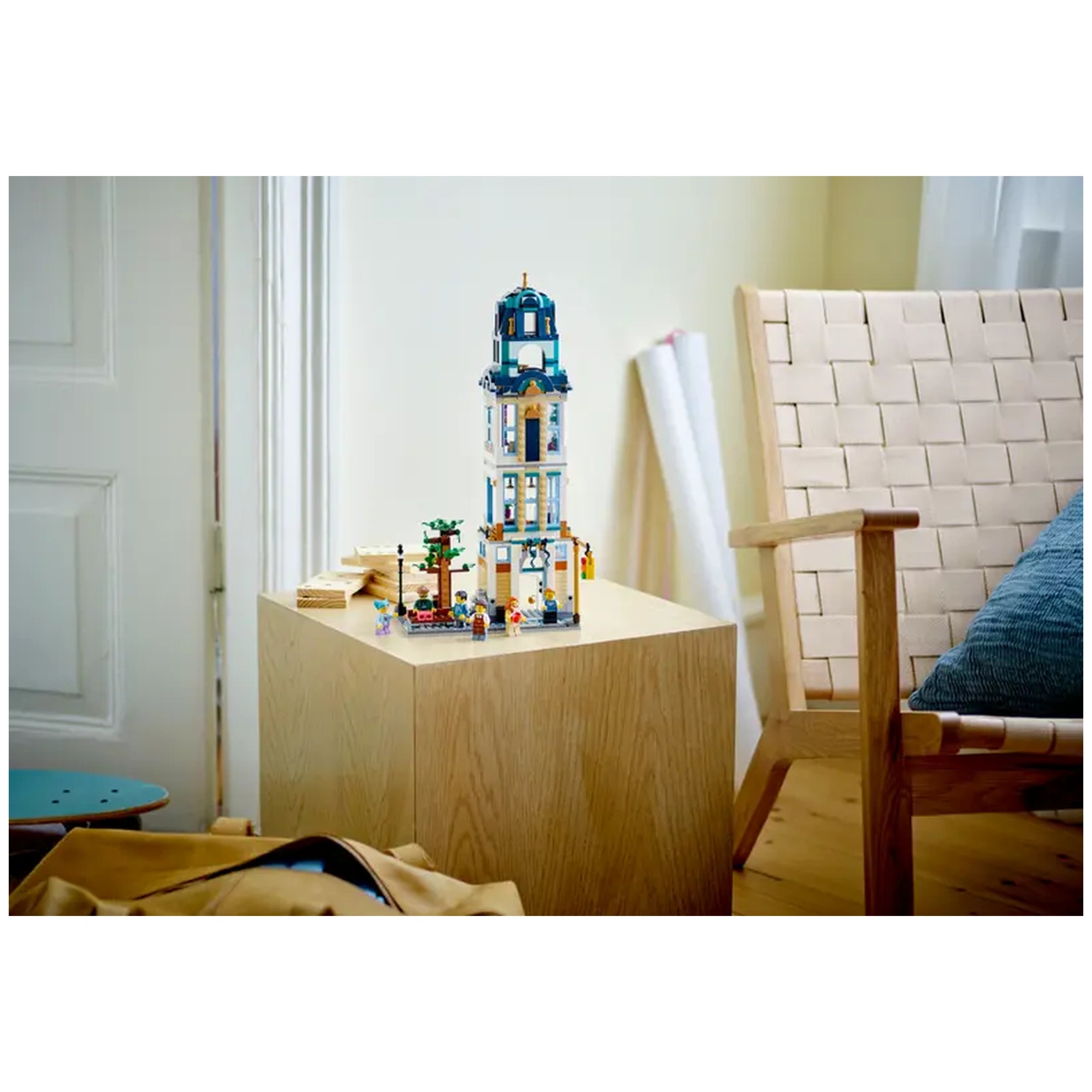 LEGO Creator 3in1 Main Street set displayed on a wooden table, featuring a colorful three-floor hotel, small trees, and minifigures, with a cozy armchair nearby.